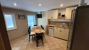 Una cocina compacta con una mesa de comedor, sillas, un refrigerador y un televisor montado en la pared.