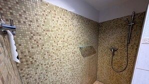 Zona de ducha con paredes de mosaico y cabezal de ducha.