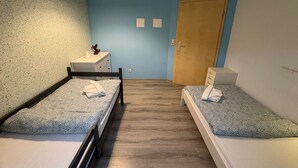 Una habitación con dos camas individuales, un escritorio pequeño, una silla, un armario y una puerta.