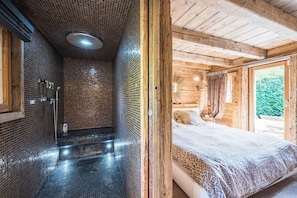 Ein Holzblock-Innenraum mit einem Badezimmer, das eine geflieste Dusche und ein Bett mit einem Bettbezug mit Leopardenmuster zeigt.