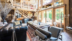 Ein geräumiger Raum mit hoher Decke, Holzbalken, einer Chandelierleuchtre, Ledermöbeln und großen Fenstern mit Blick ins Freie.