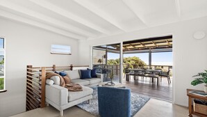 A modern living room with a sofa, coffee table, and a view of the outdoor patio area. - The Surf Nook | Walk to Beach | Family Friendly (Gracetown)