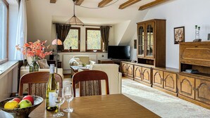 Uma sala de estar acolhedora com uma mesa de jantar de madeira, cadeiras, uma televisão e um armário.