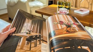 Uma revista sobre uma mesa com cadeiras, um vaso com flores e uma televisão ao fundo.