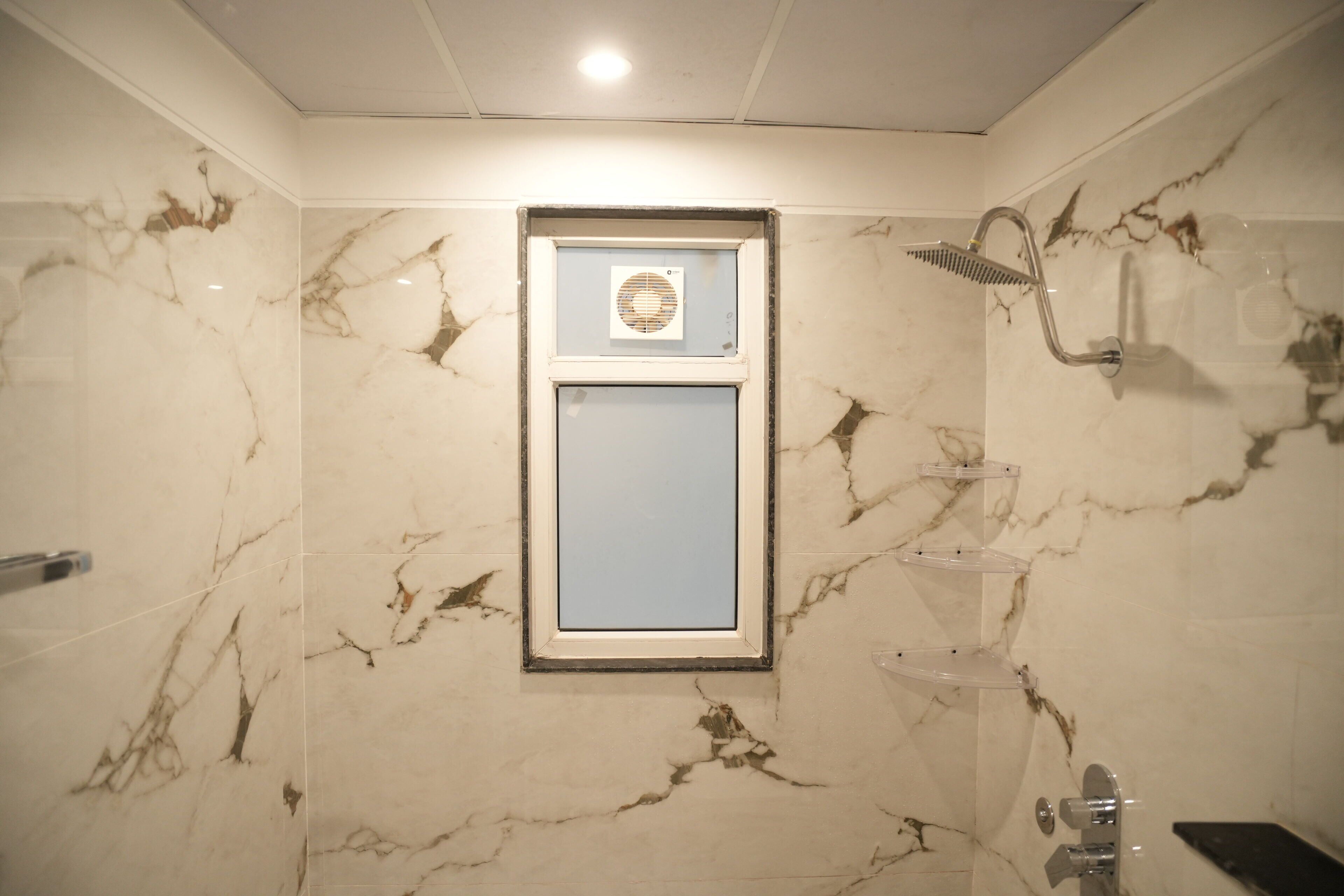 Une salle de bain avec des murs en marbre, un miroir encadré, une douche avec un pommeau de douche amovible et un porte-serviettes.