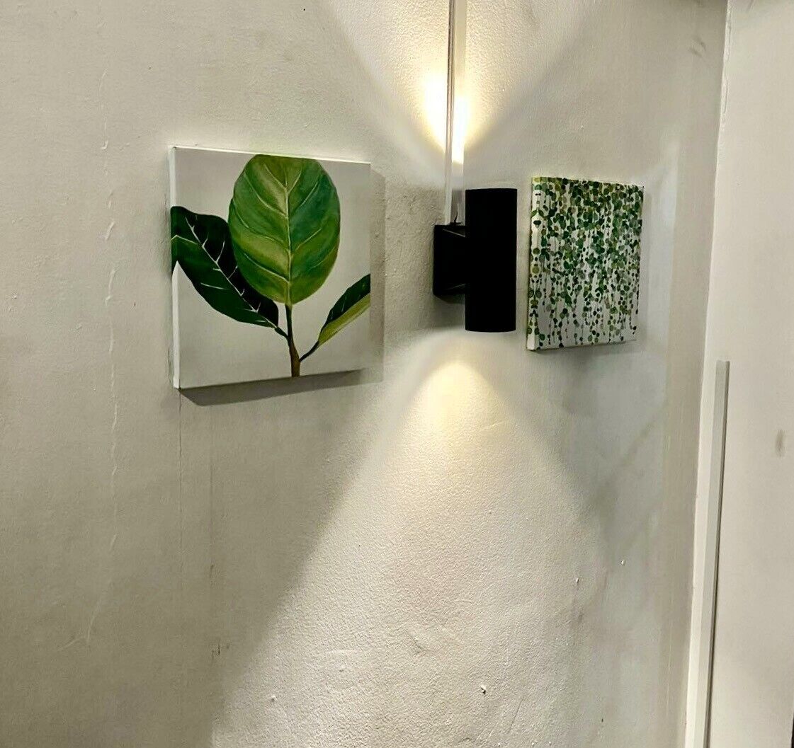 Una pared con dos cuadros enmarcados: uno con una hoja y otro con un diseño verde.