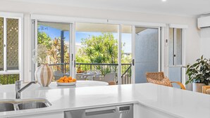 A modern kitchen with a large island, a built-in dishwasher, and a view of a balcony with outdoor furniture. - The Beach House in Shelly Beach (Caloundra Region)