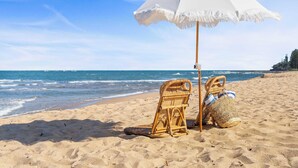 A beach scene with a white umbrella, wicker chairs, and a woven bag on the sand. - The Beach House in Shelly Beach (Caloundra Region)