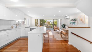 A modern kitchen with white cabinets, a central island, and a dining area with a wooden floor. - The Beach House in Shelly Beach (Caloundra Region)