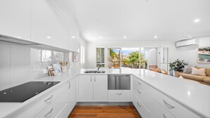A modern kitchen with white cabinetry, a black stovetop, and a dishwasher. - The Beach House in Shelly Beach (Caloundra Region)