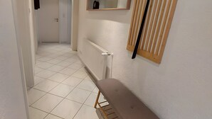 Ein Flur mit einer Bank, einem Heizkörper, einem Fenster aus Holzleisten und einem Spiegel an der Wand.