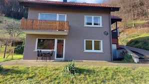 Ein zweistöckiges Haus mit Balkon, Schornstein und einem kleinen Anbau.