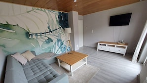 Ein modernes Wohnzimmer mit einem grauen Sofa, einem Holztisch und einem großen abstrakten Gemälde an der Wand.