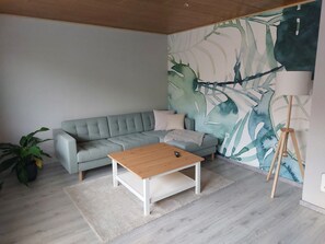 Olohuoneessa on harmaa sohva, puinen sohvapöytä, lattiavalaisin ja suuri abstrakti seinämaalaus.