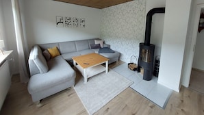 Een moderne woonkamer met een grijze bank, een houten salontafel en een zwart houtkacheltje.