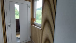 Een kamer met een houten plafond, een witte deur met raam, een radiator en uitzicht op groen.