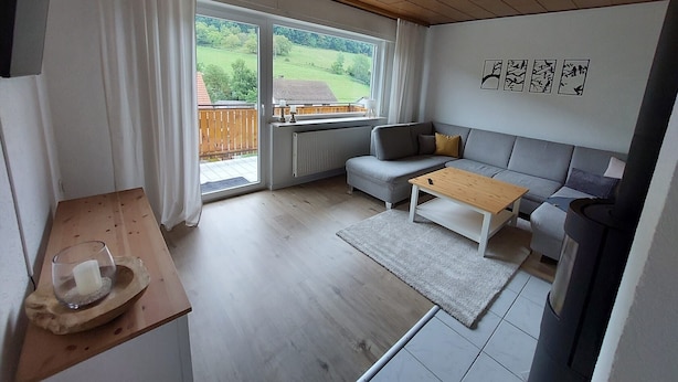 Een moderne woonkamer met een bank, een salontafel, een open haard en uitzicht op een tuin door grote ramen.