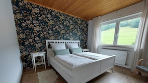 Een slaapkamer met een bed, een nachtkastje, een raam met uitzicht op het landschap en een houten plafond.