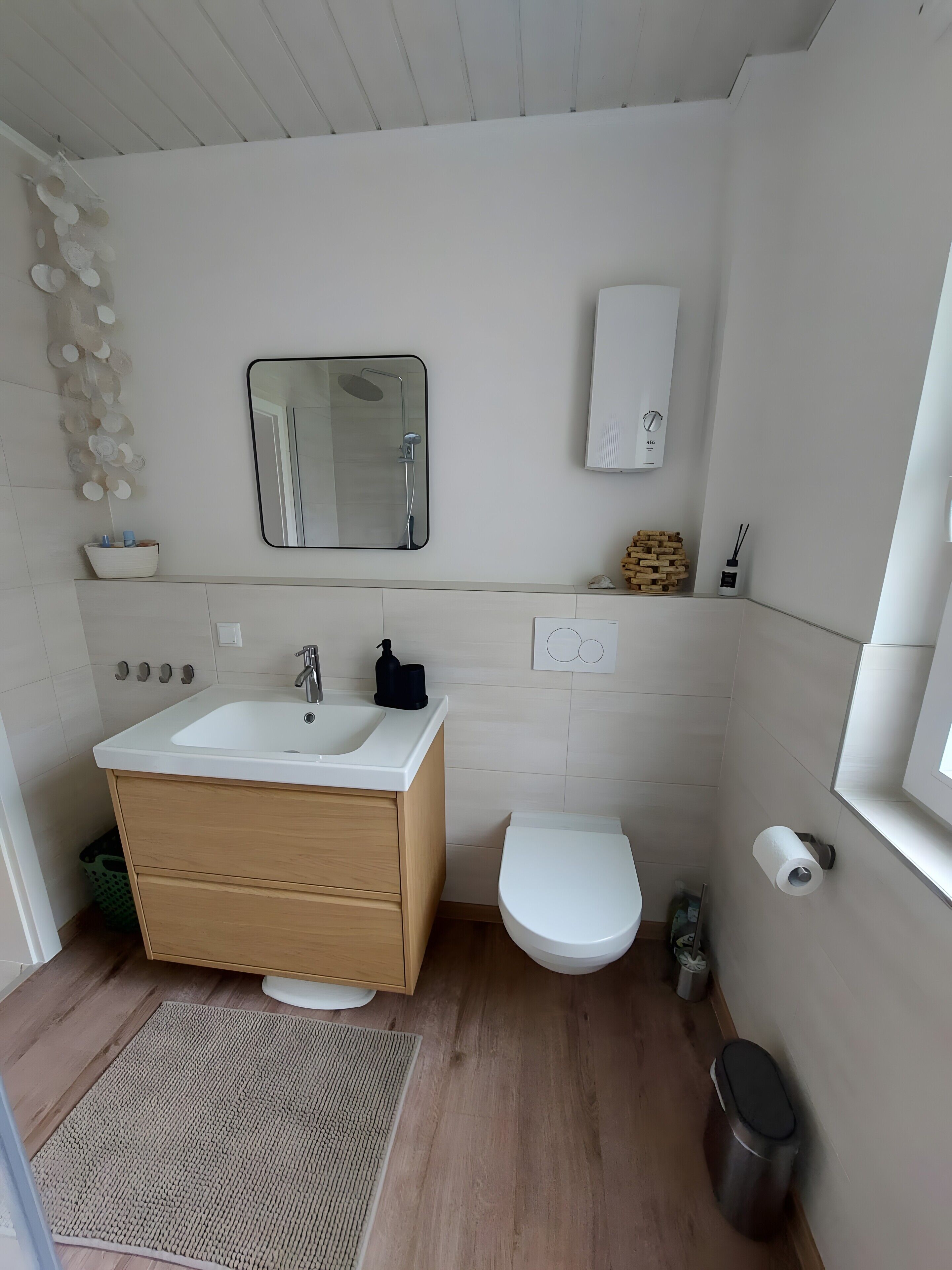 Ein modernes Badezimmer mit Waschbecken, Spiegel, Toilette und einem kleinen Mülleimer.