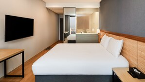A modern hotel room with a large bed, a flat-screen TV mounted on the wall, a wooden nightstand, and a desk. - Nova Stay Gangneung (Gangneung)