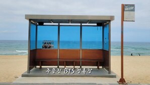 A bus stop with a bench and a sign, located on a beach with the ocean in the background. - Nova Stay Gangneung (Gangneung)