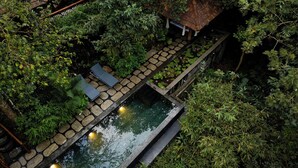 Un ponte in pietra che sovrasta un'acqua specchiante, circondato da vegetazione lussureggiante e un piccolo padiglione.