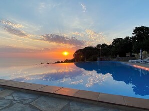Una piscina con vista al atardecer, escalones de piedra que bajan a la piscina y sillones de descanso a orillas de la piscina.