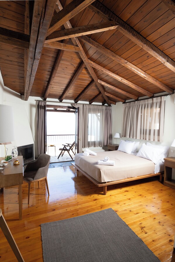 Un dormitorio con techo de madera, una cama, un escritorio con silla y un balcón con cortinas.