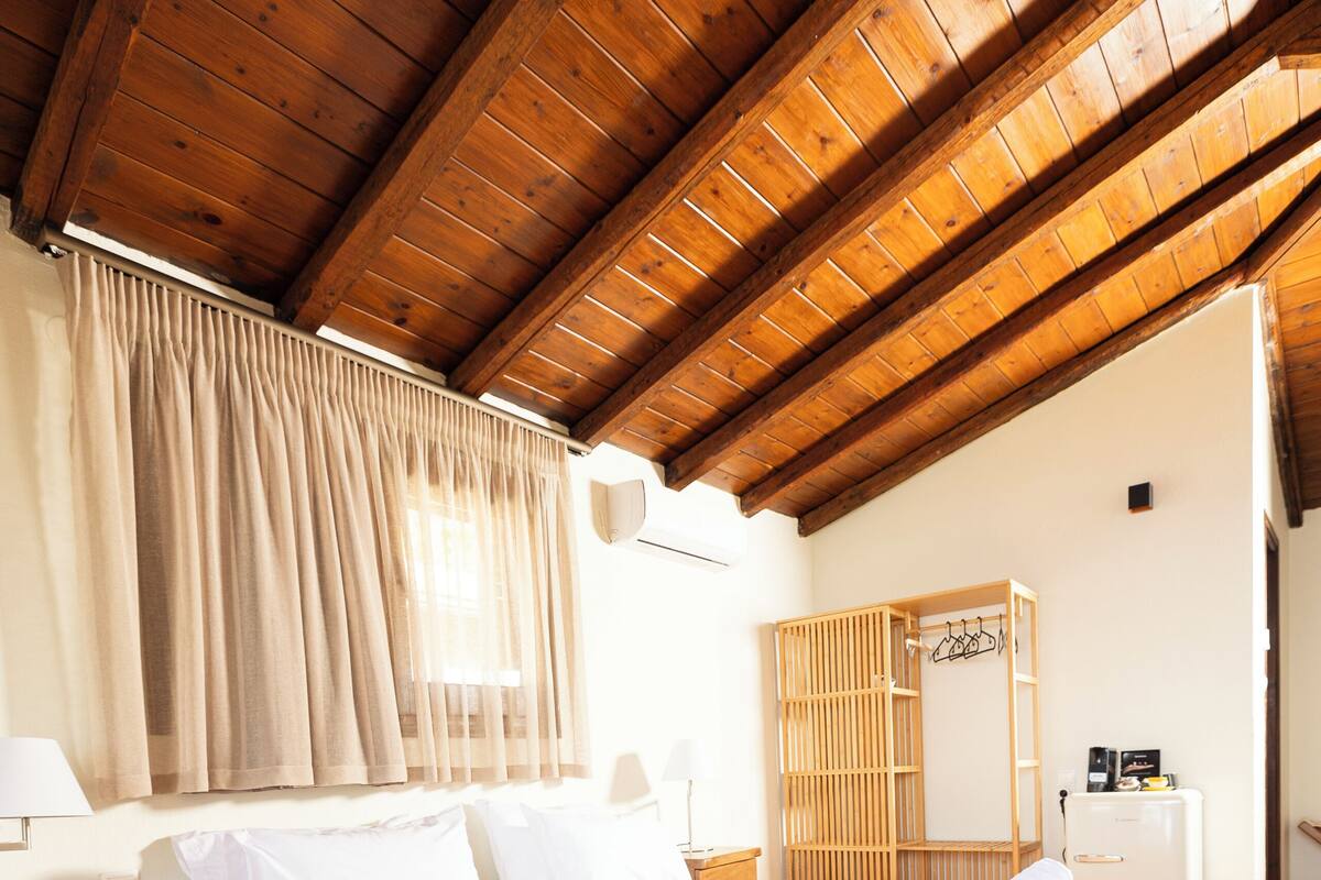 A wooden-framed room with a bed, a wardrobe, and a small table with a lamp.