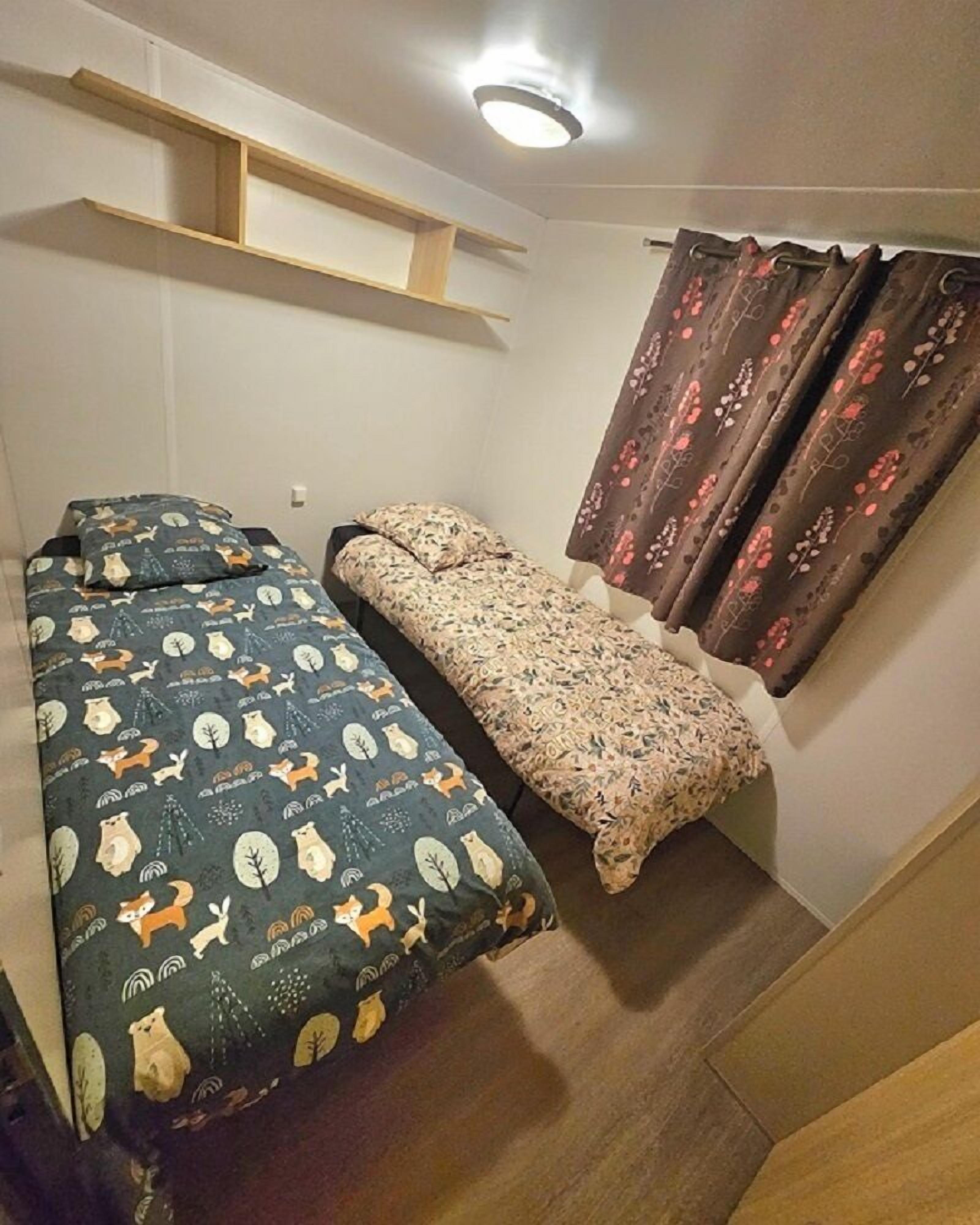 A small room with a bed, a bench, and a window with curtains.
