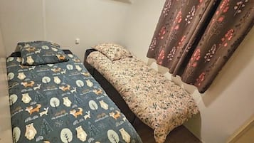 A small room with a bed, a bench, and a window with curtains.