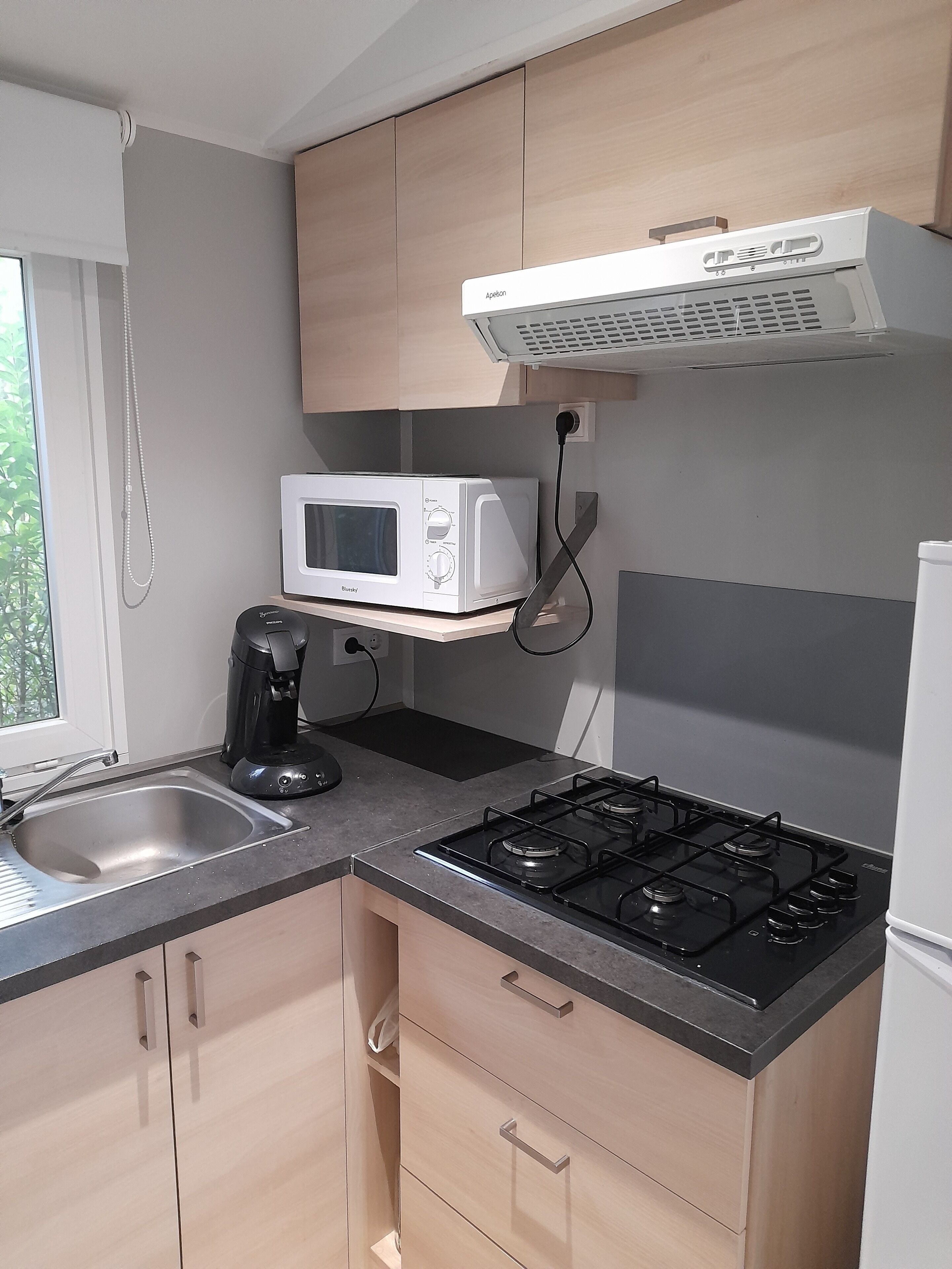 Una cocina compacta con estufa a gas, microondas, cafetera y armarios de madera.