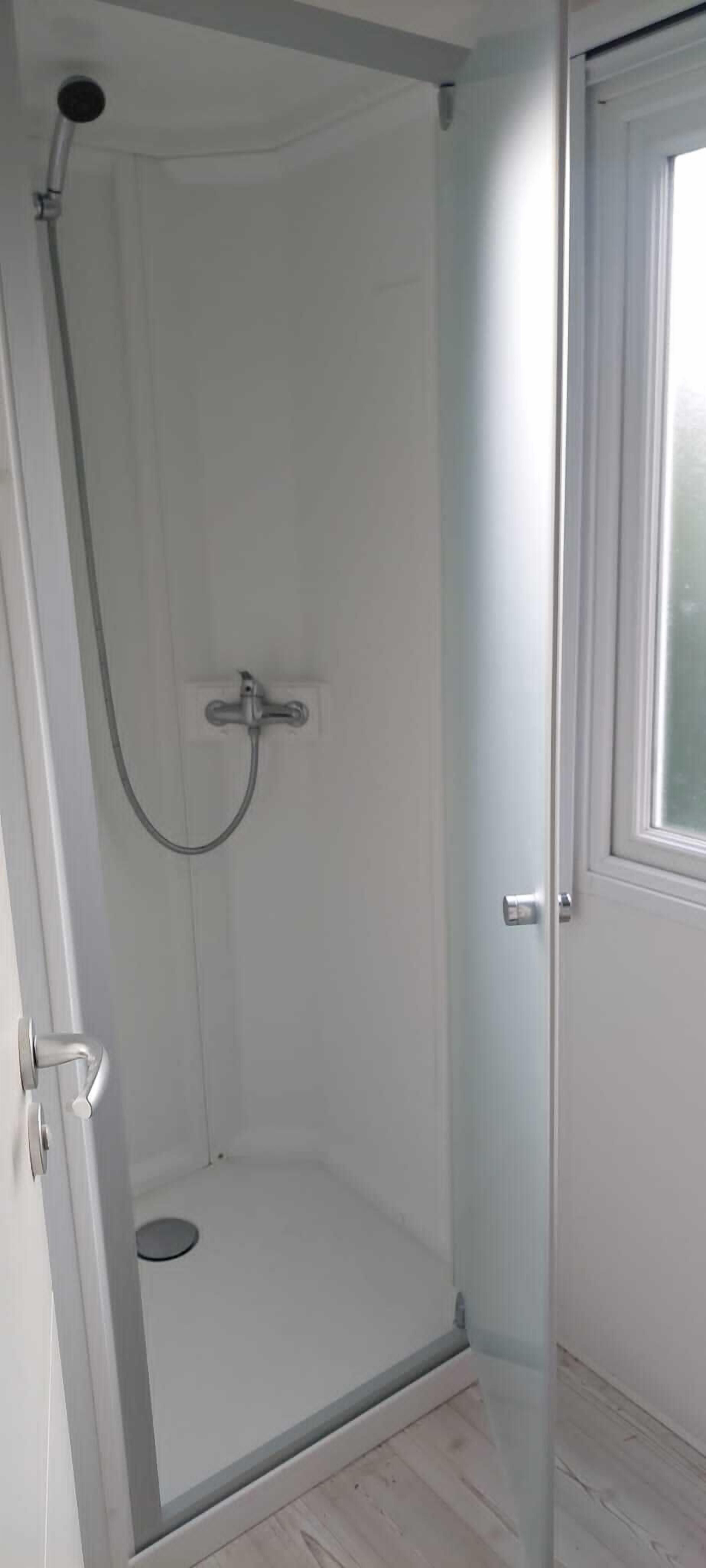 A walk-in shower with a glass door, a showerhead, and a control panel.