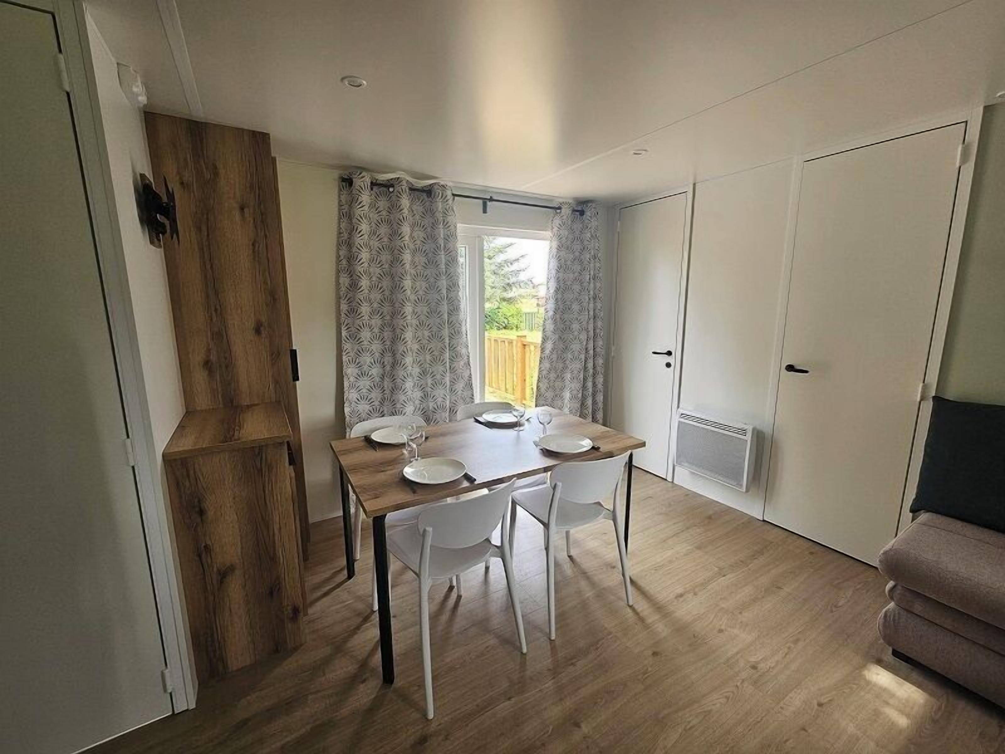 Een eethoek met een houten tafel, witte stoelen en een raam met gordijnen met een patroon.