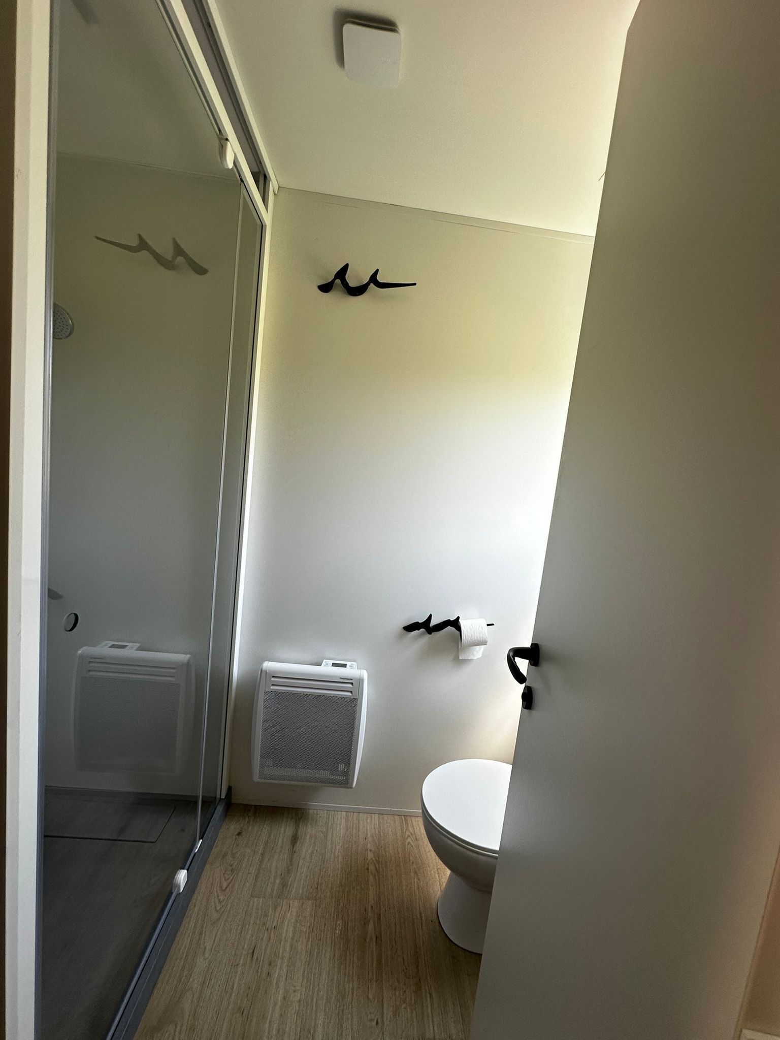 A modern bathroom with a glass shower enclosure, a toilet, and a wall-mounted towel rack.