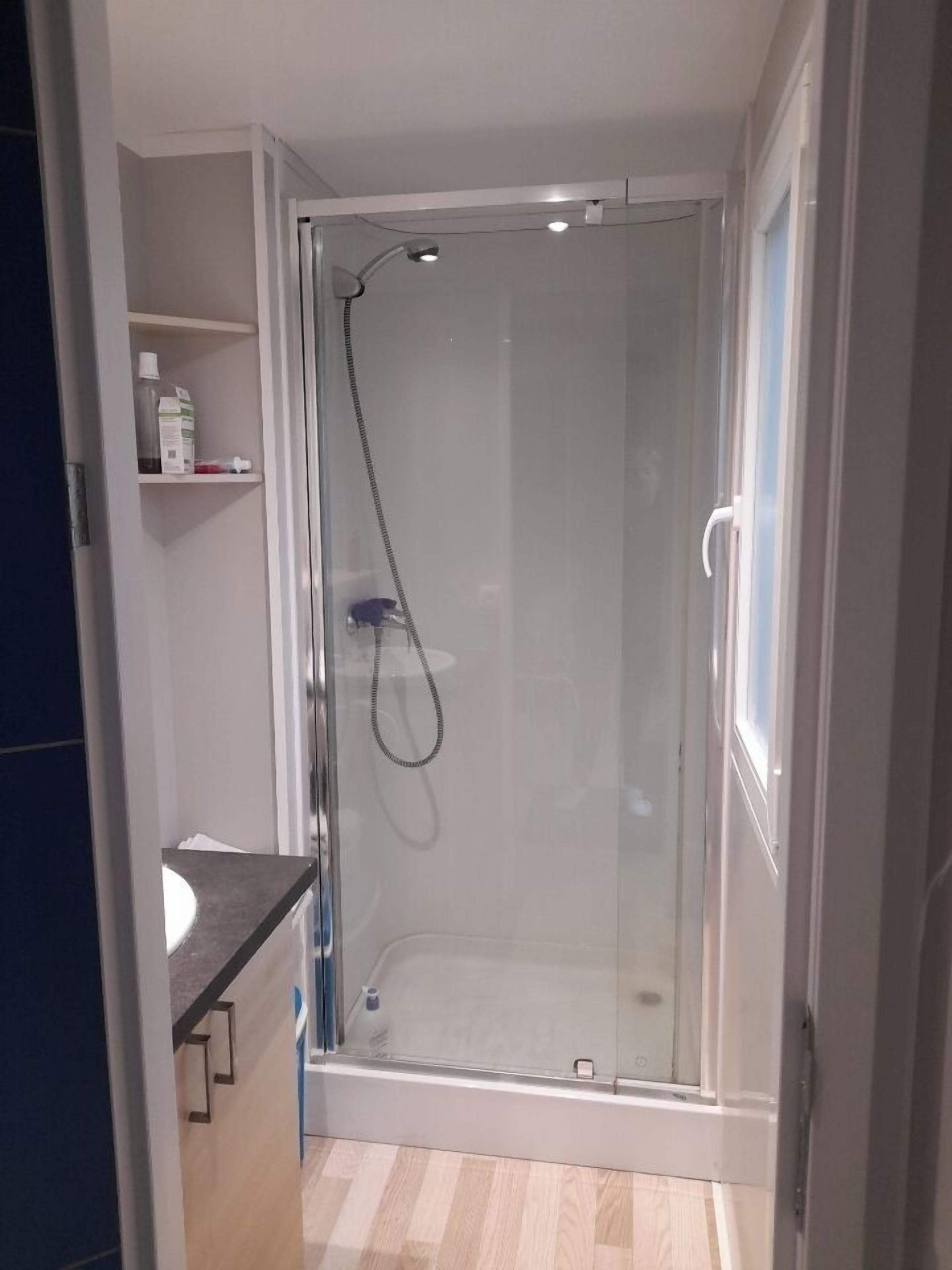 A modern bathroom with a glass-enclosed shower, a white sink, and a small shelf with toiletries.