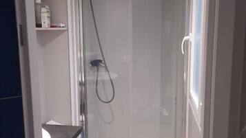 A modern bathroom with a glass-enclosed shower, a white sink, and a small shelf with toiletries.