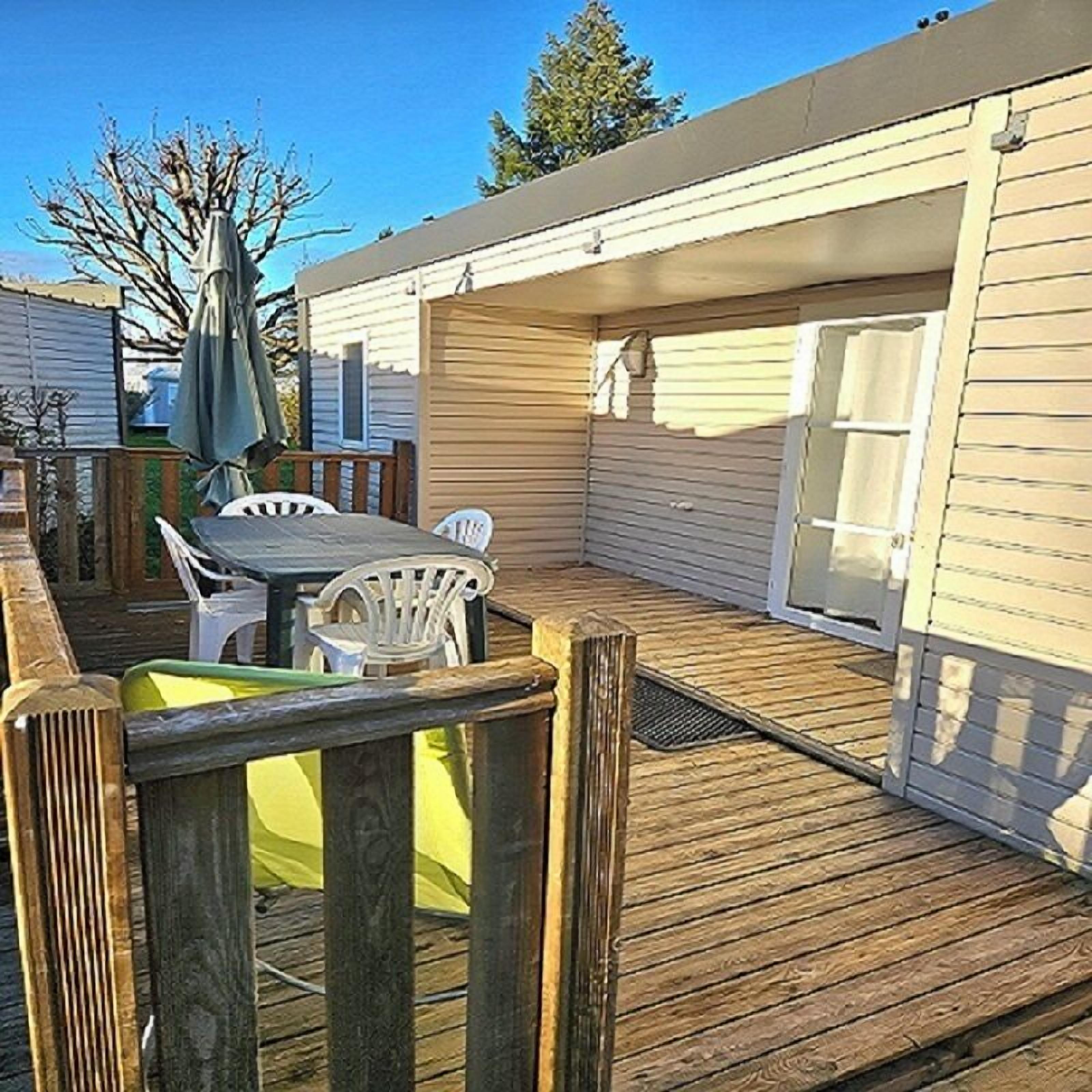 A wooden deck with a table and chairs, a covered patio area, and a sliding door leading to a garage.