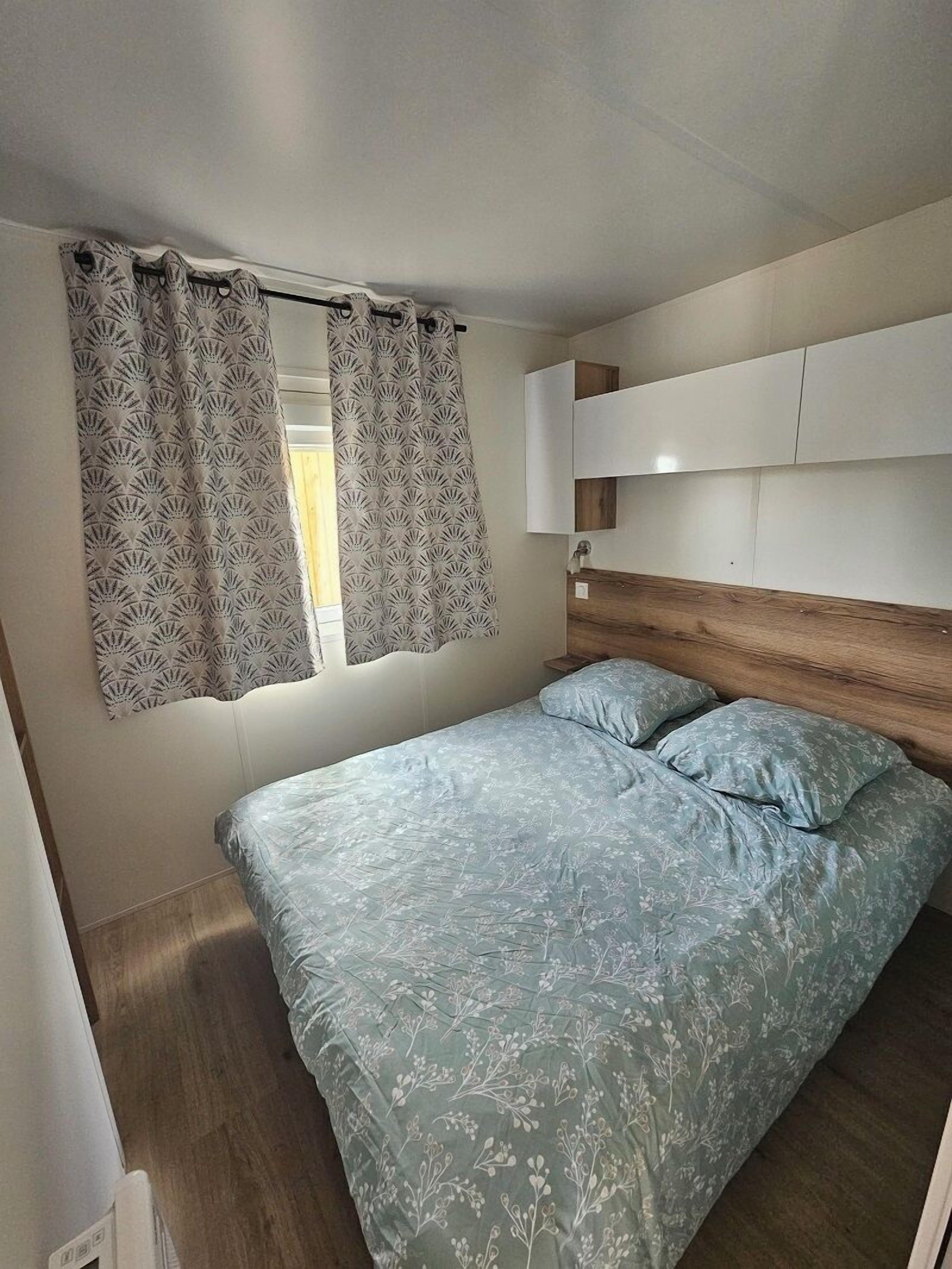 Un dormitorio con cama, cortinas, cabecero de madera y armarios empotrados.