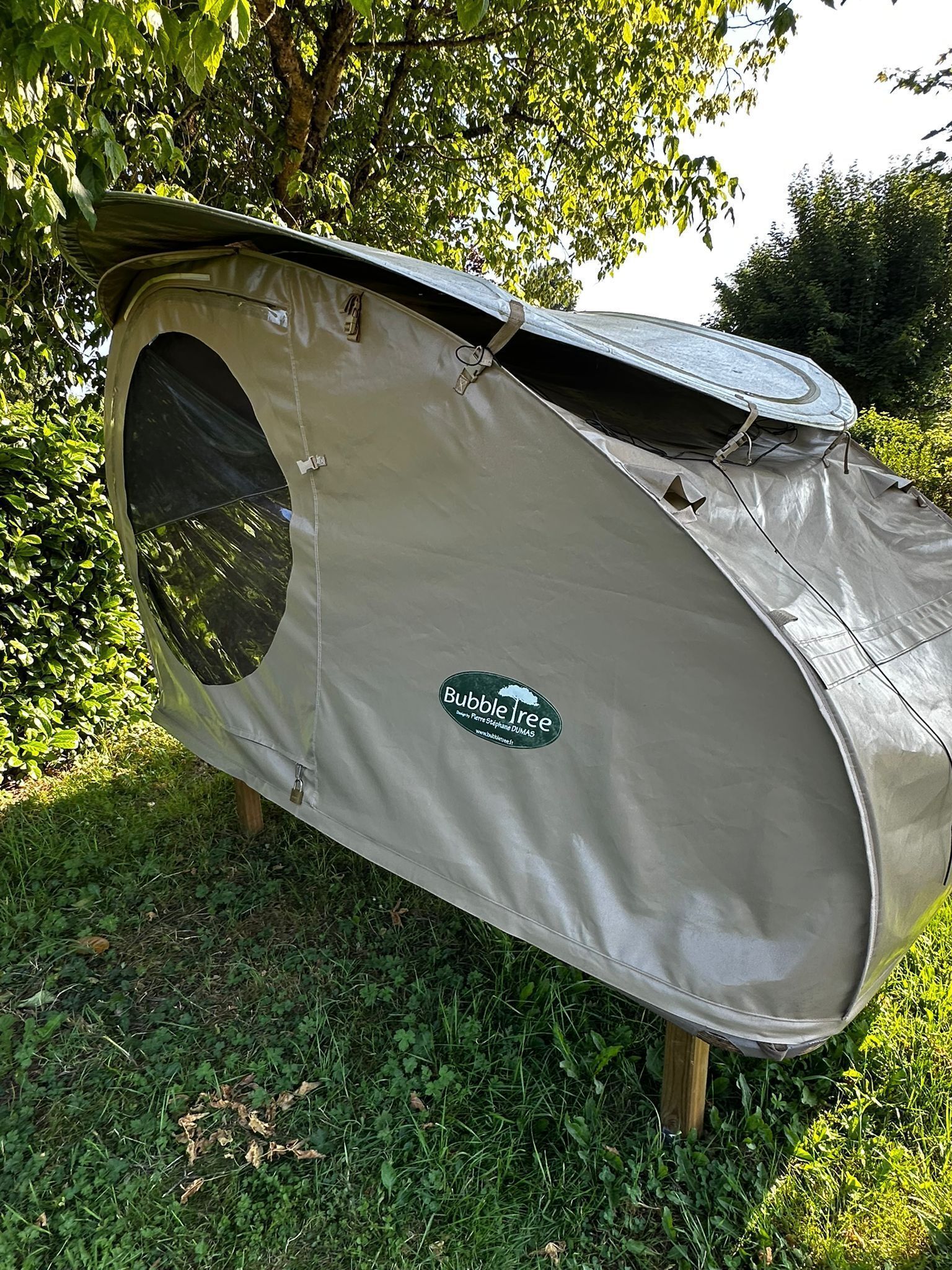 A tent with a logo, standing on wooden legs in a grassy area with trees.