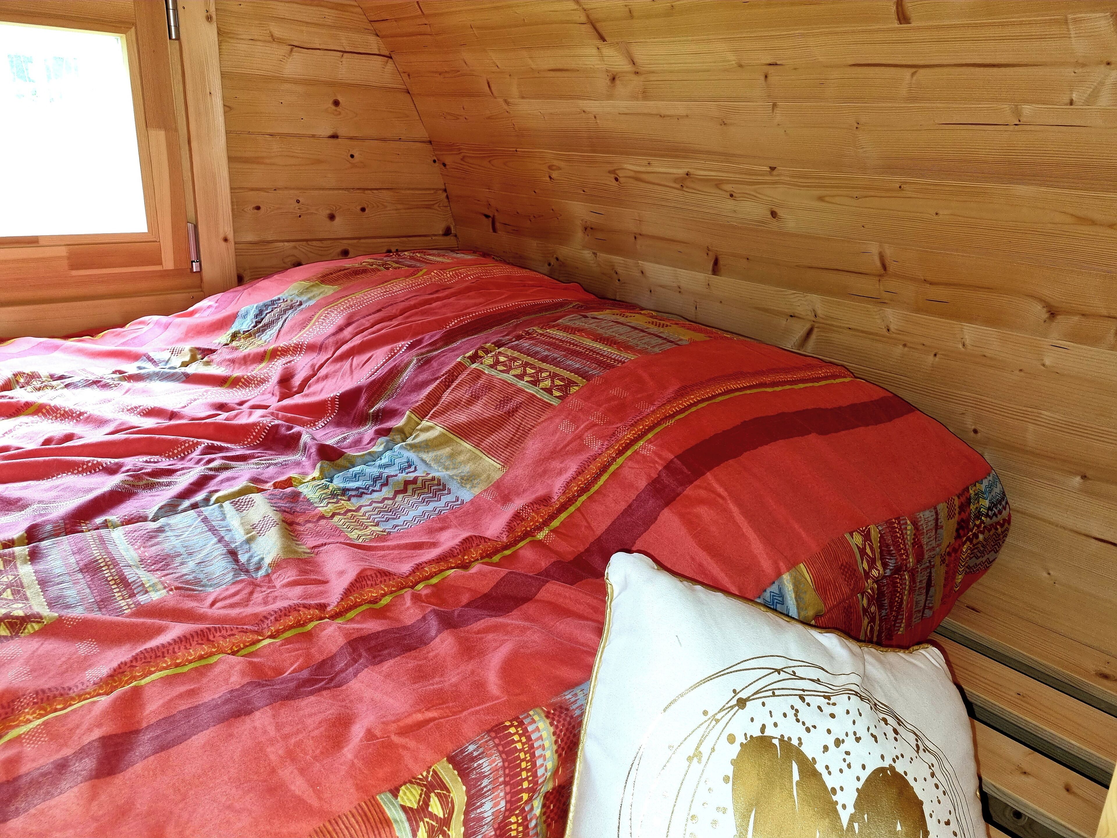 Een houten kamer met een bed, voorzien van een kleurrijke quilt en een decoratief kussen.