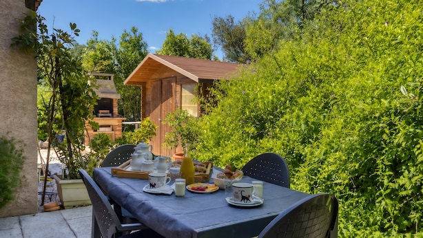 A table set outdoors with breakfast items, surrounded by greenery and a wooden building in the background. - Villa Désirée Agde – Guest Room with Private Terrace and Garden (Agde)