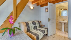 A room with a wooden ceiling, a sofa with patterned cushions, a small table, a white door leading to a bathroom with a sink and mirror. - Villa Désirée Agde – Guest Room with Private Terrace and Garden (Agde)