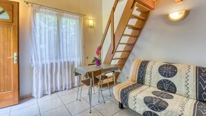 A room with a wooden staircase, a bed with patterned bedding, a table with a chair, and a window with sheer curtains. - Villa Désirée Agde – Guest Room with Private Terrace and Garden (Agde)