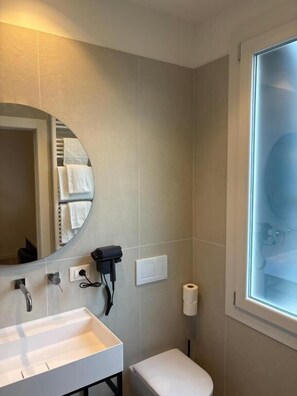 Ein Badezimmer mit einem weißen Waschbecken, einem Spiegel, einem Handtuchhalter, einer Toilette und einem Fenster mit blickdichter Verglasung.