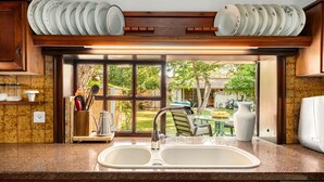 A kitchen with a double sink, wooden cabinets, and a view of a backyard with a table and chairs. - Relax in a Garden Oasis by Sea N' Rent (Nahariya)