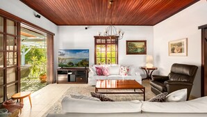 A spacious living room with a wooden ceiling, a white sofa, a brown leather chair, and a TV on a stand. - Relax in a Garden Oasis by Sea N' Rent (Nahariya)