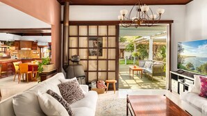 A modern living room with a sofa, a coffee table, and a TV. There is a kitchen in the background with wooden cabinets and a dining area. - Relax in a Garden Oasis by Sea N' Rent (Nahariya)