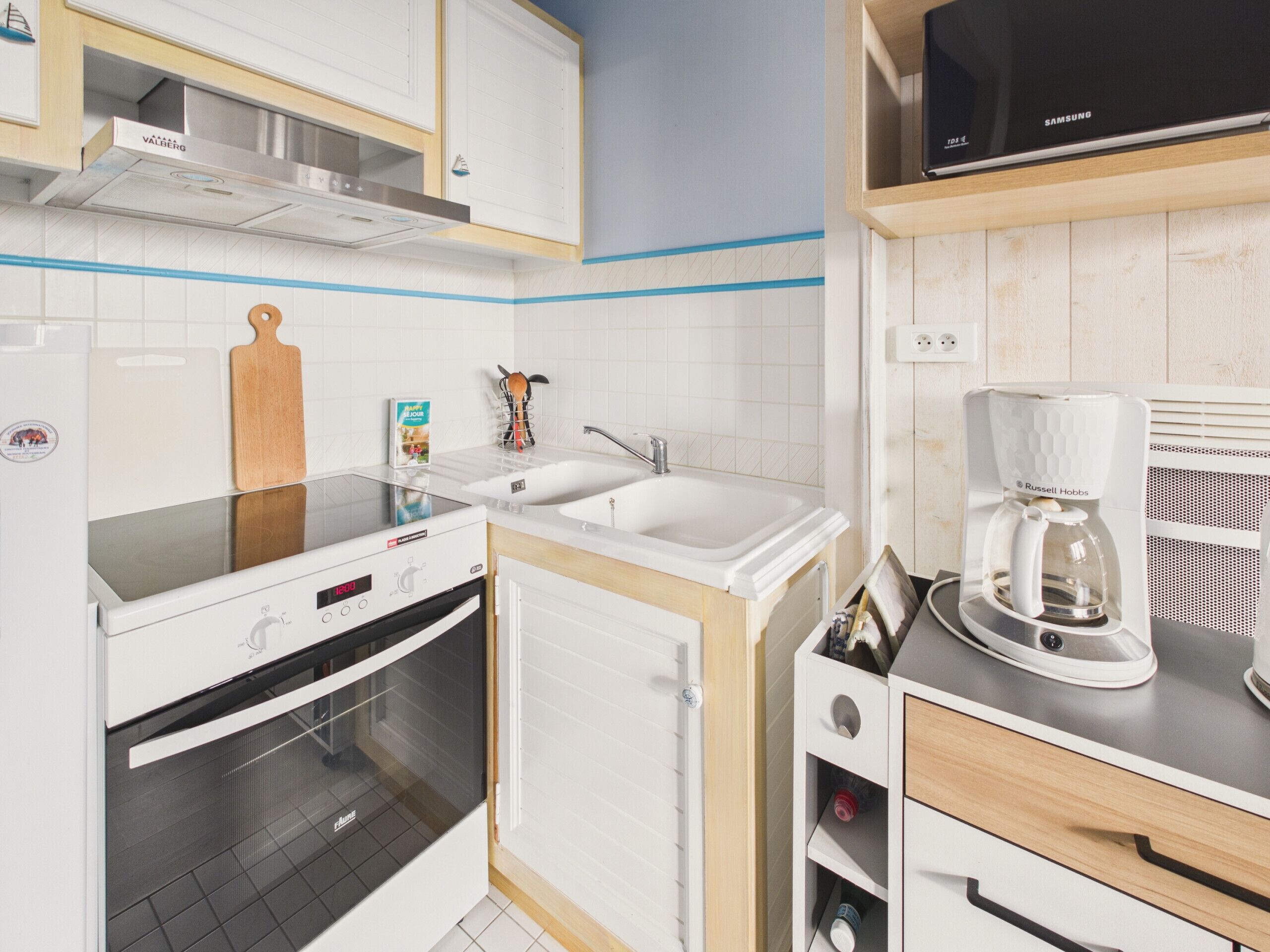 A modern kitchen with white cabinetry, a built-in oven, a double sink, and a coffee maker.