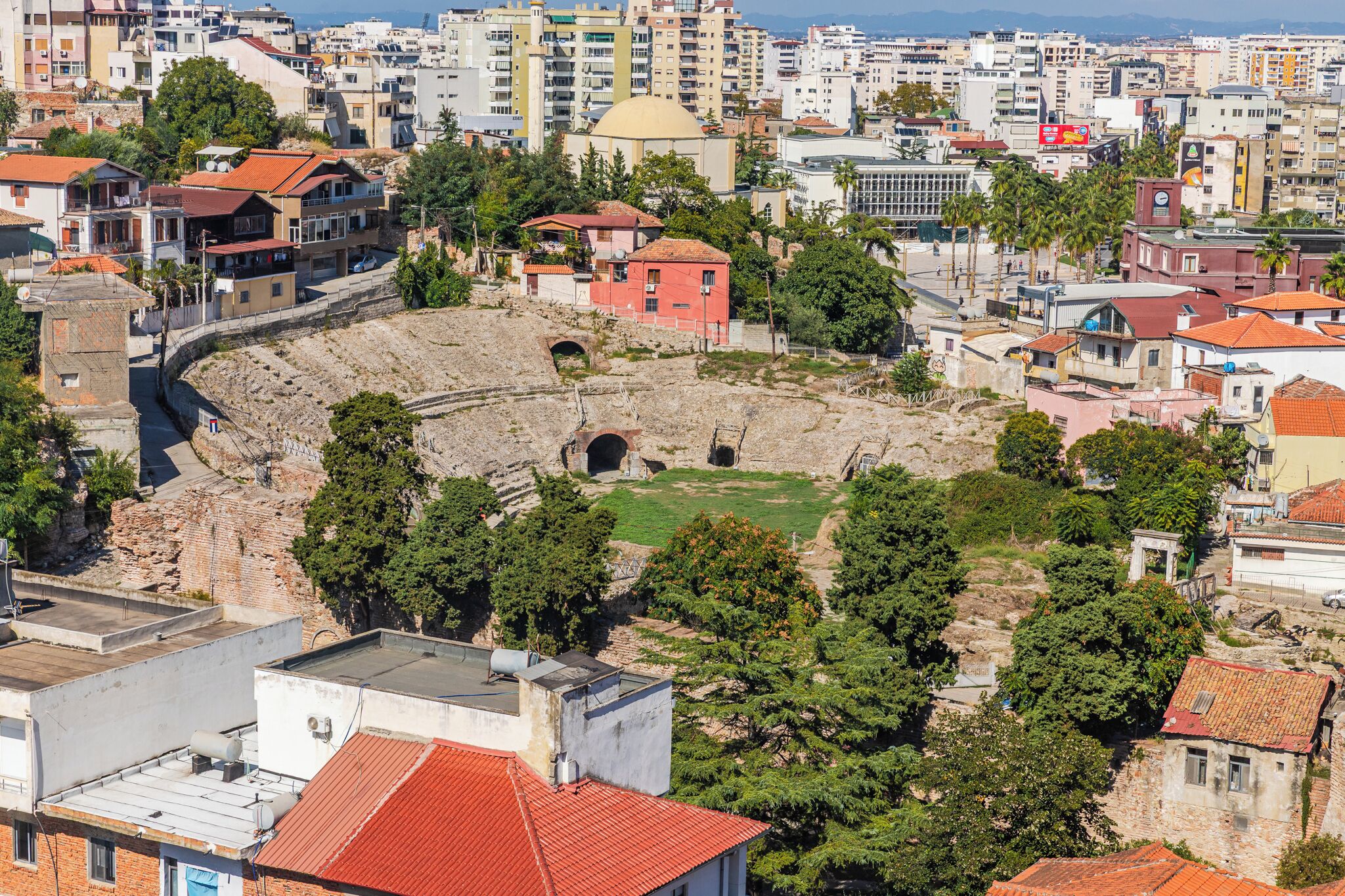 An ancient amphitheater surrounded by modern buildings and trees.
